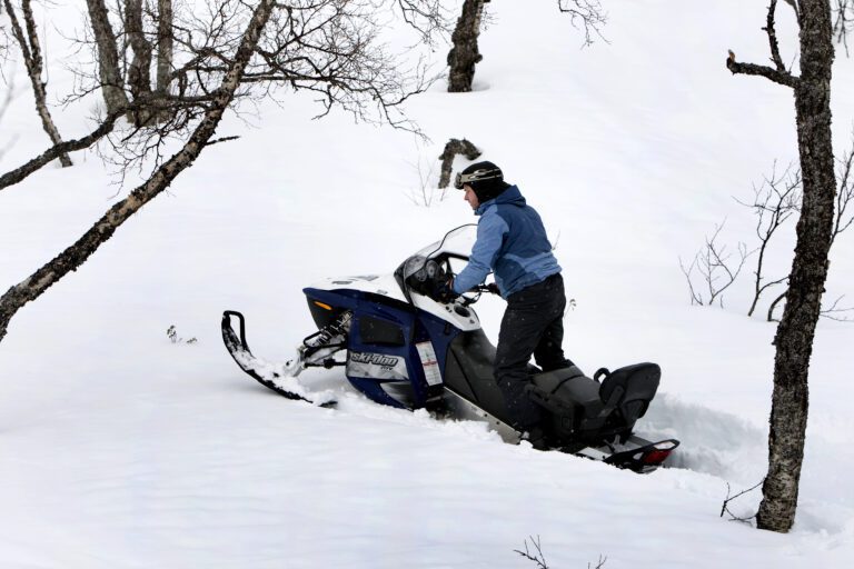 Mann kjører snøscooter som setter seg fast i løs snø.