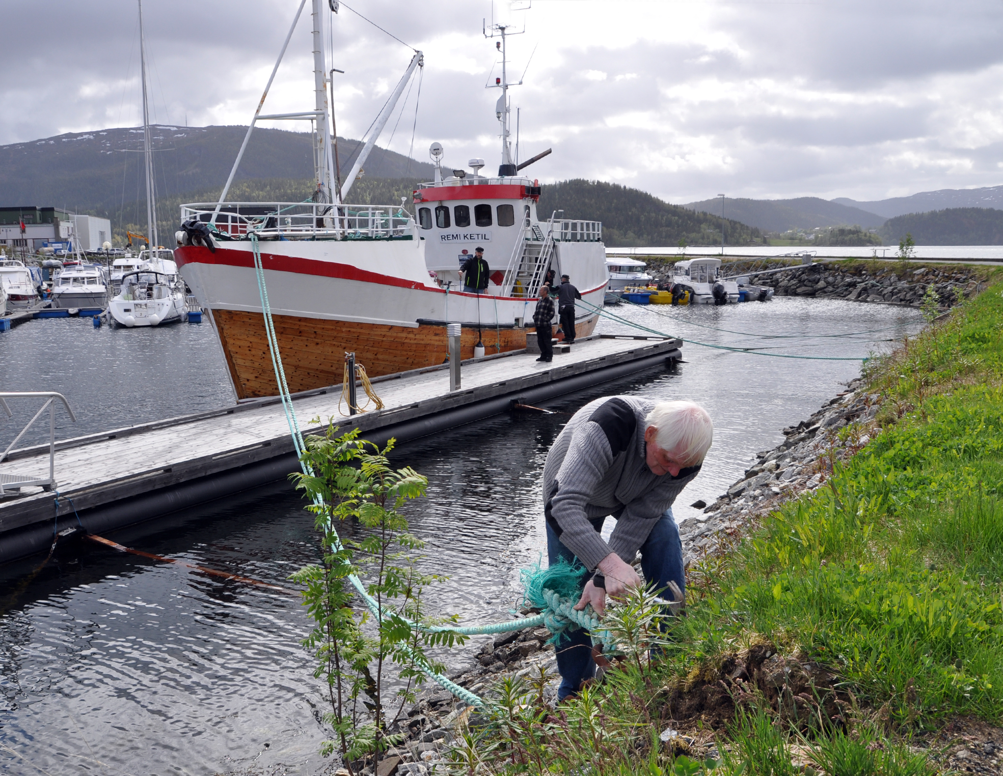 orbjørn Skjæran gjør laus en av tampene som holder Remi Ketil trygt på plass i marinaen.|Remi Ketil siger fint fra flytebrygga i marinaen på Hemnesberget.|For egen maskin siger veteranbåten Remi Ketil pent og pyntelig ut fra marinaen.|Egil Jenssen og Børge Gullesen i hver sin "bukserbåt" følge vaktsomt|Sigurd Nermark haler på land trossa Oddbjørn Nilsen og Åge Karlsen har slengt på kaia.|Stein Dahlberg følger nøye med fra det åpne vinduet på broen.